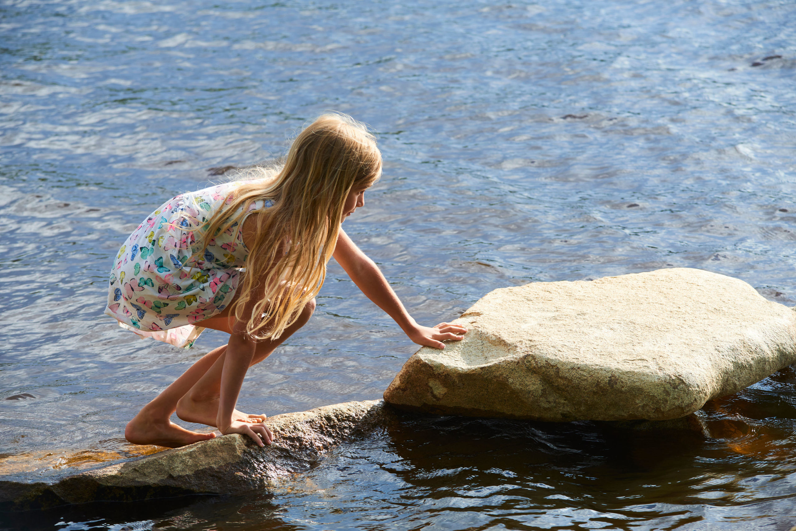 Young girl playing on the rocks in the water.